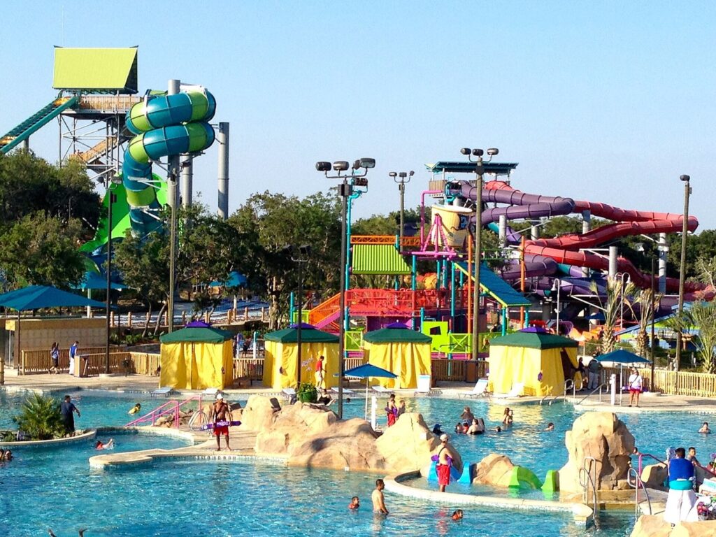 Colorful water slide towers and a shallow lagoon with swimmers and shade cabanas at Aquatica San Antonio