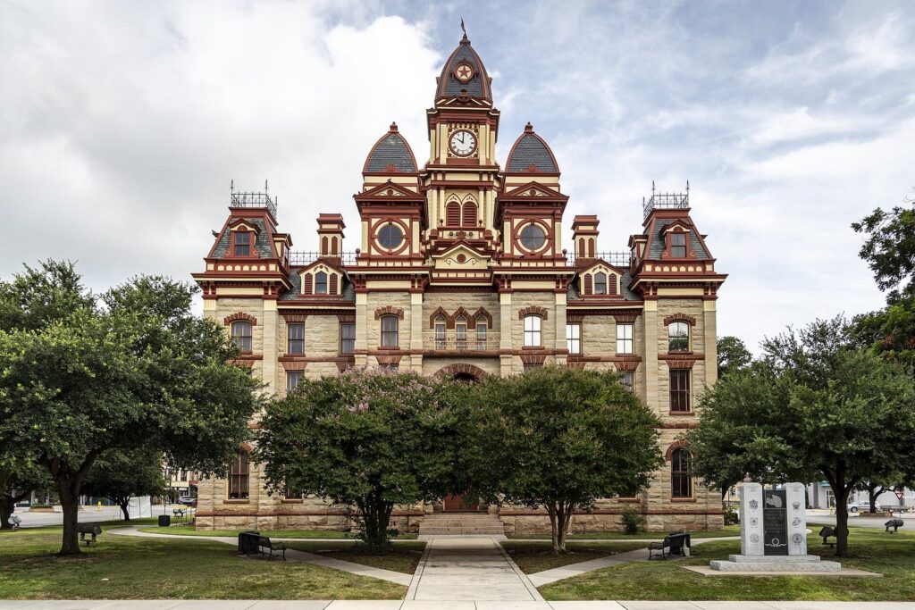 The ornate Caldwell County Courthouse in Lockhart with its central clock tower, mansard roofs and red trim behind shade trees