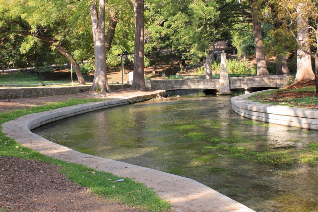 The clear, spring-fed Comal River curving between stone walls and shade trees in Landa Park, New Braunfels
