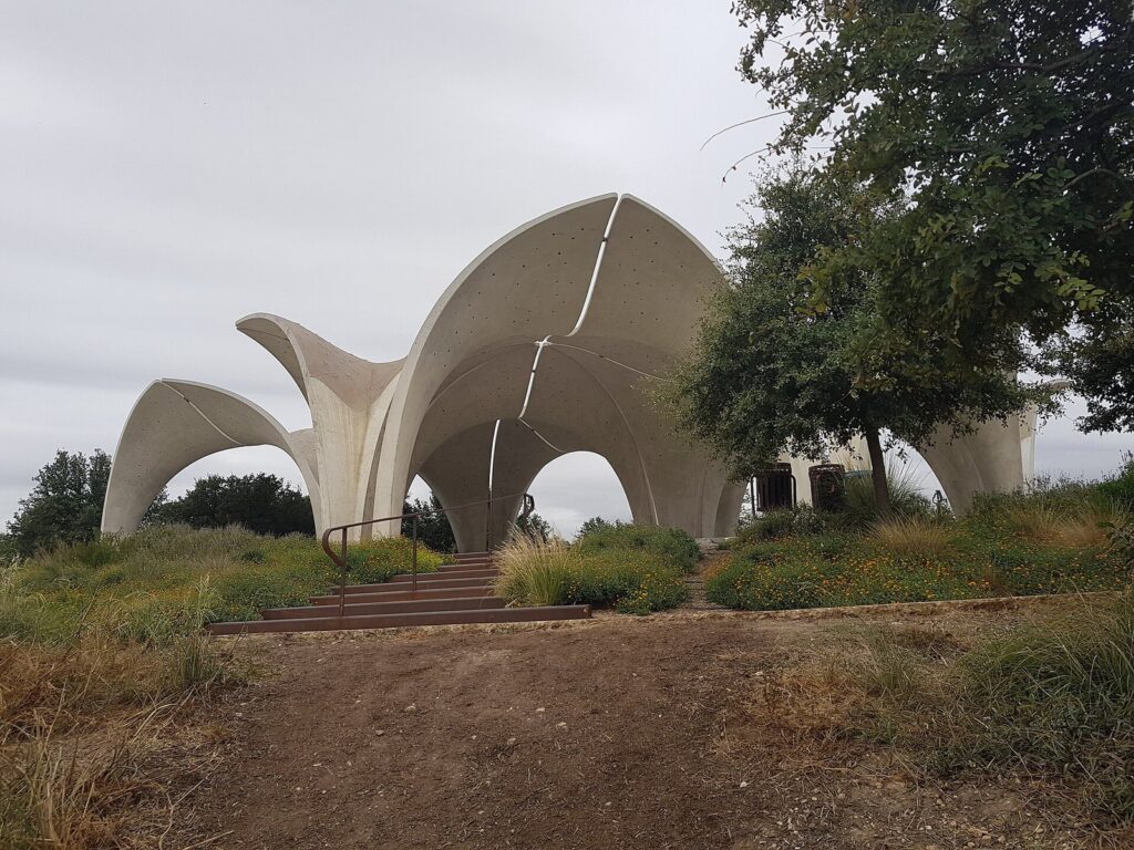 The white concrete petal-shaped pavilions of Confluence Park rising above native grasses and oak trees on a cloudy day
