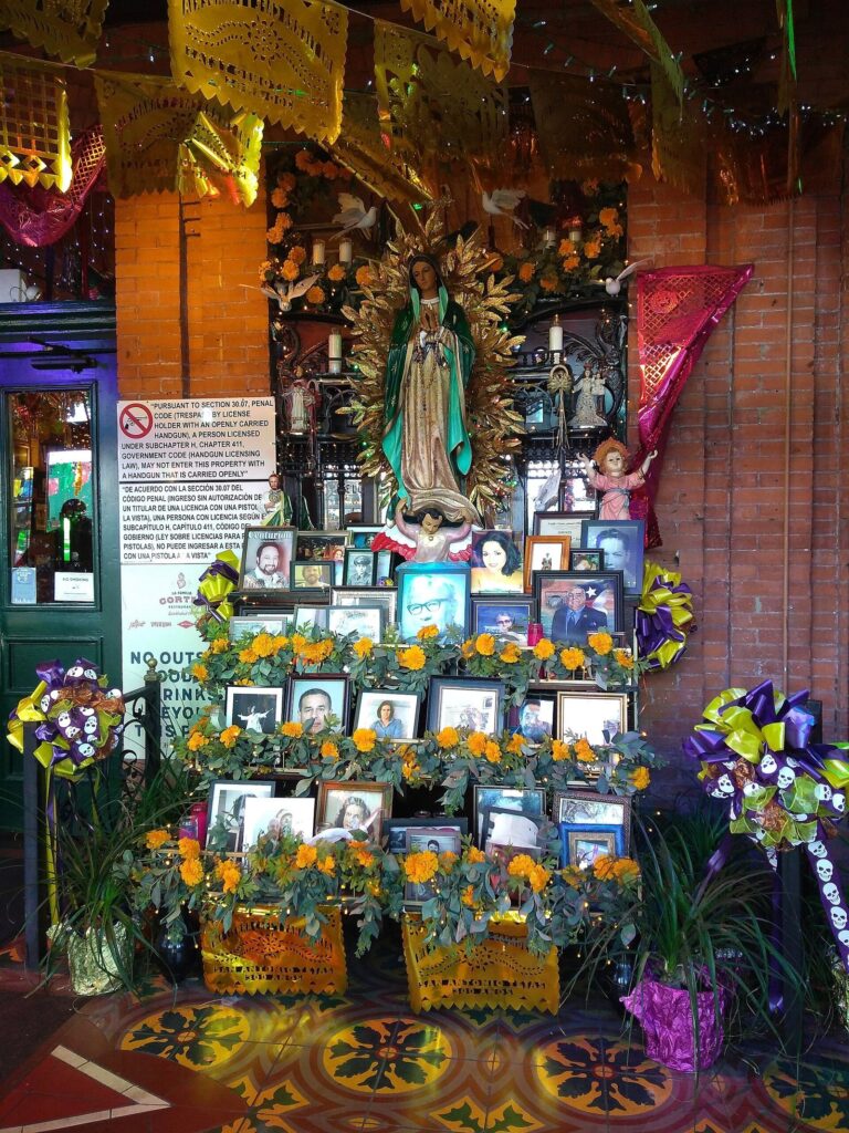 A tall Day of the Dead altar decorated with marigolds, candles, photographs and an image of the Virgin of Guadalupe at Mi Tierra