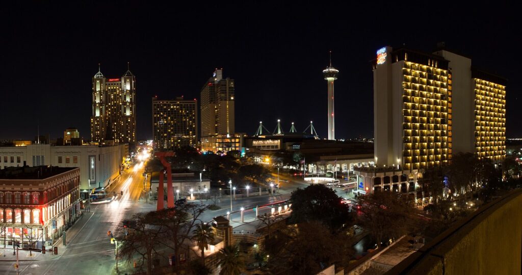 Downtown San Antonio at night from above, with lit hotel towers, the Tower of the Americas and streets glowing below