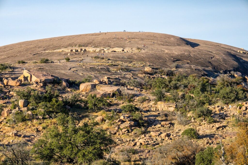 Hikers dotting the bare pink granite dome of Enchanted Rock above scrub and boulders, one of the best day trips from San Antonio