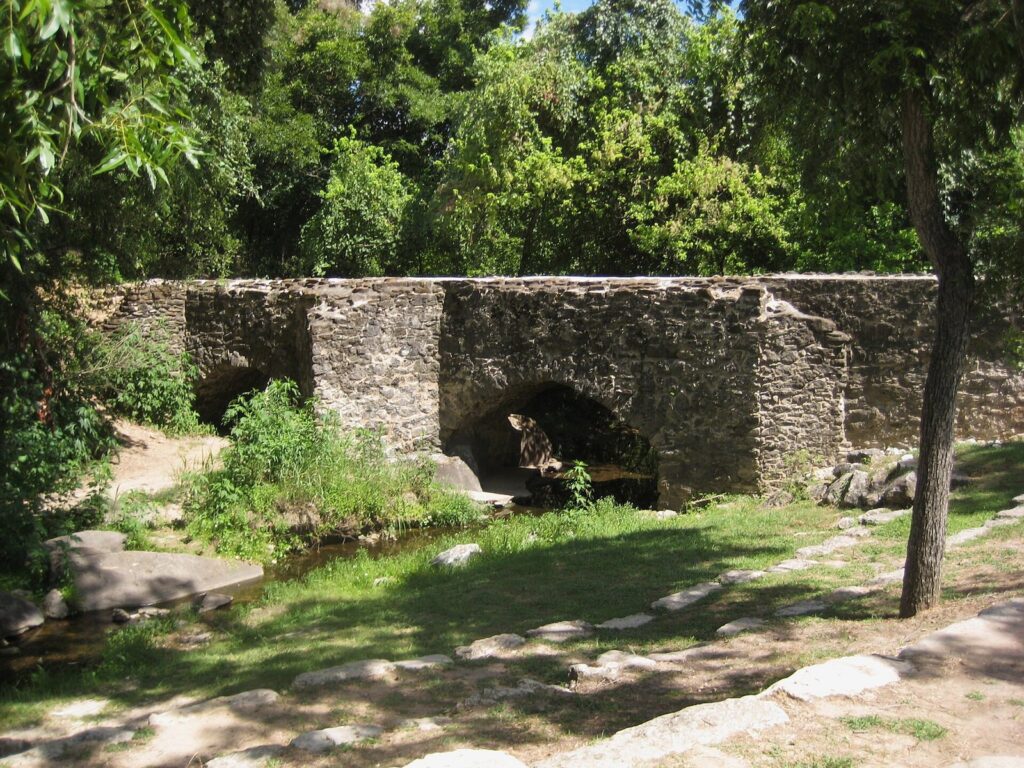 The stone Espada Aqueduct carrying an irrigation ditch over a creek on low arches, among green trees