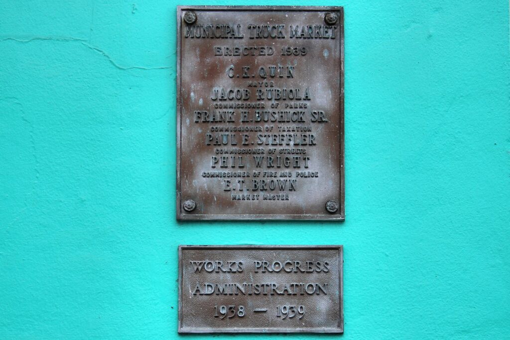 Bronze plaques on a turquoise wall at Market Square recording the Municipal Truck Market, erected 1939, and the Works Progress Administration, 1938 to 1939
