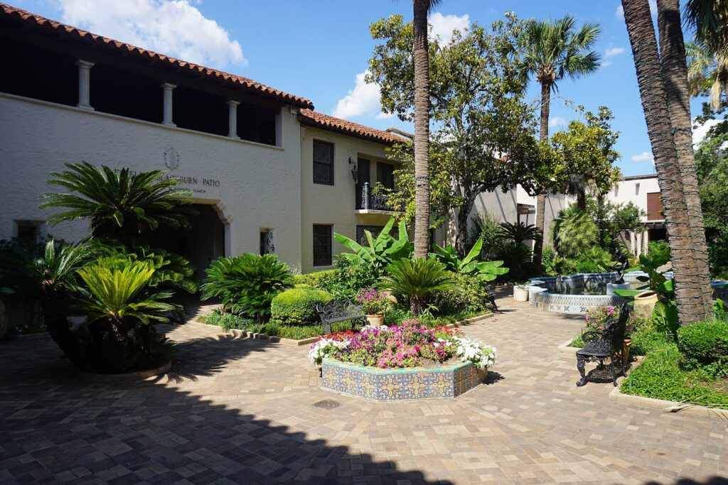 The McNay Art Museum's courtyard with palms, tiled planters full of flowers and a fountain framed by the white stucco mansion
