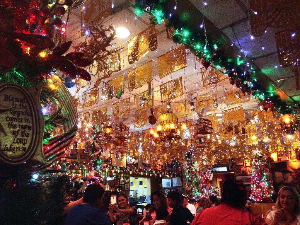 Diners under strings of colored lights, papel picado and hanging ornaments inside Mi Tierra Café y Panadería at Market Square