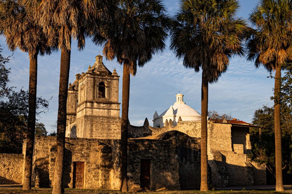 Mission Concepción's twin bell towers and stone walls framed by tall palms at sunset, a free stop in any San Antonio budget travel guide
