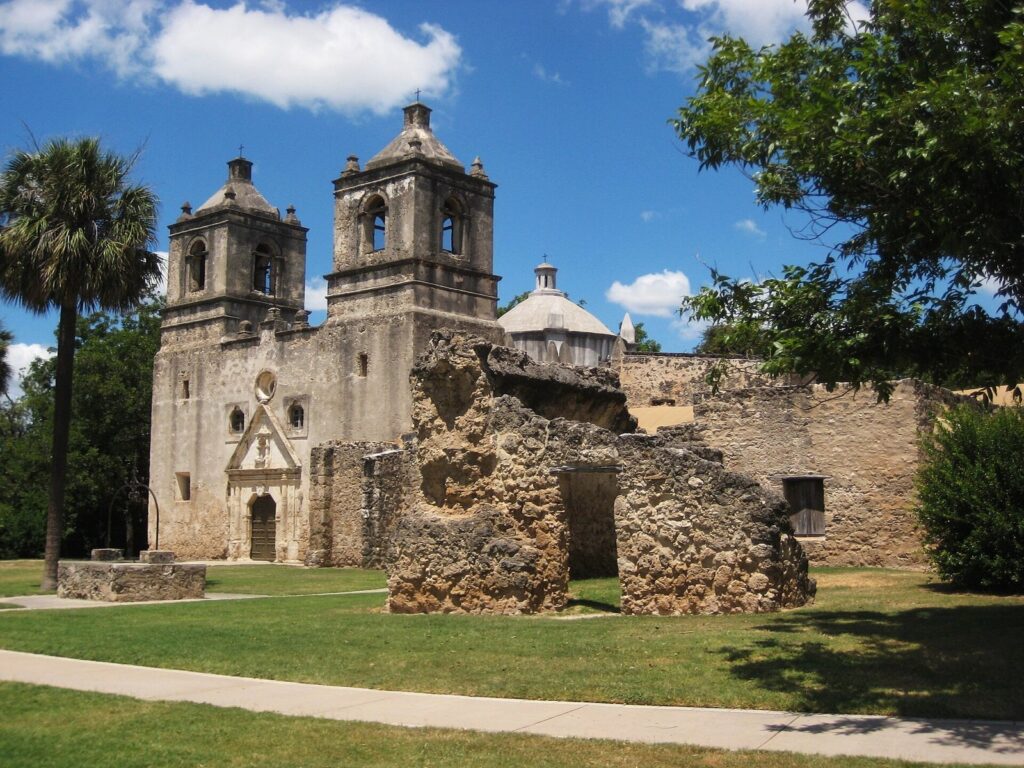 The twin bell towers, dome and weathered stone front of Mission Concepción, one of the San Antonio Missions, under a blue sky