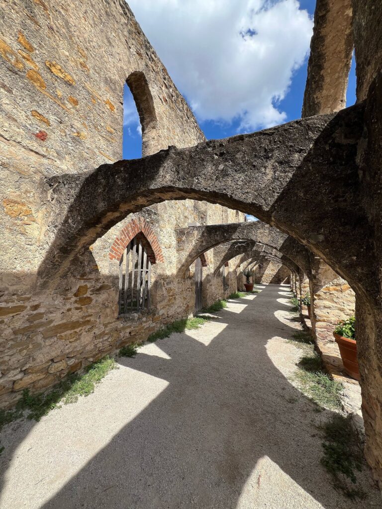 A gravel path running beneath the stone arches of the cloister walkway at Mission San José