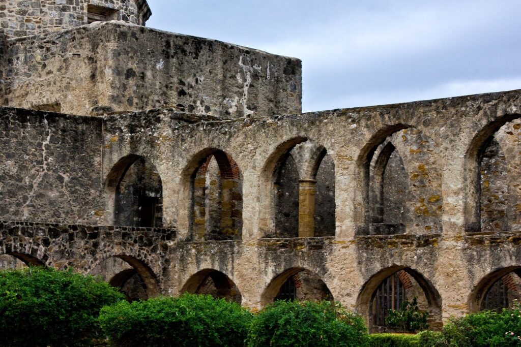 Weathered limestone arches of the convento ruins at Mission San José, with green shrubs in front