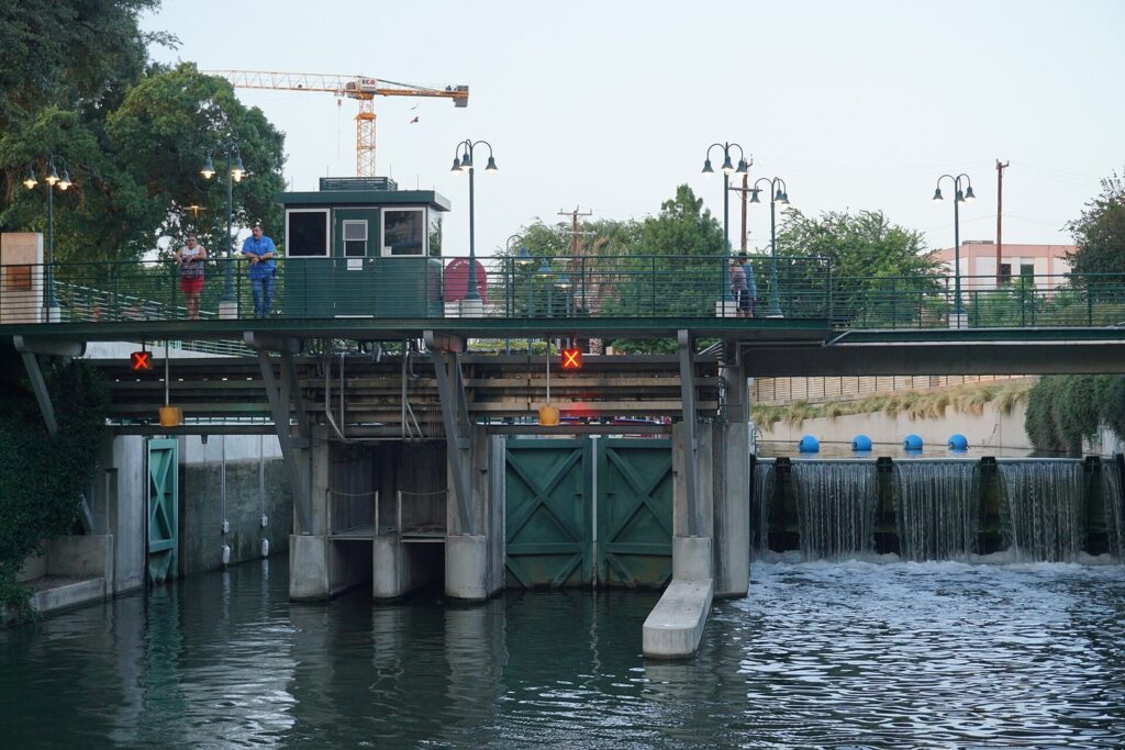 Green lock gates and control house of the Brooklyn Avenue lock and dam on the Museum Reach, with water spilling over the dam