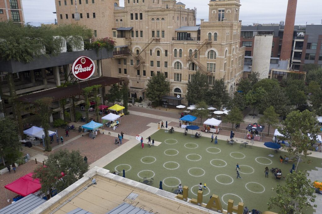 Aerial view of farmers market tents on the plaza at the Pearl in San Antonio, below the brick brewhouse and a Pearl sign