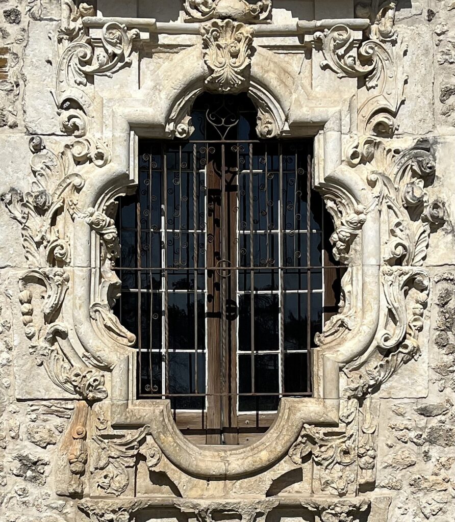 The ornately carved stone frame of the Rose Window at Mission San José, set in a rough limestone wall