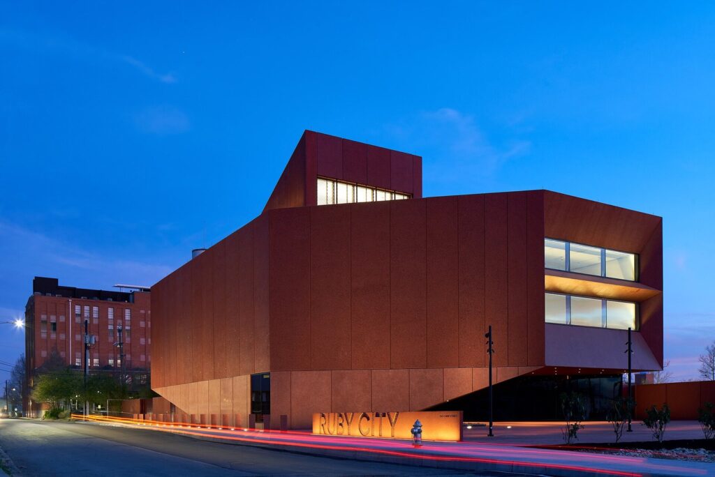 Ruby City's angular building clad in deep red concrete panels, lit at dusk against a blue sky