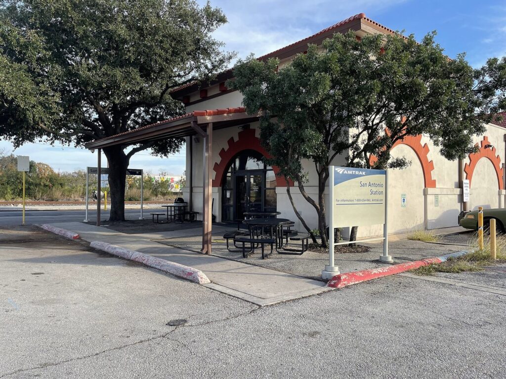 The small Amtrak station building in San Antonio with a covered platform, picnic tables and live oak trees