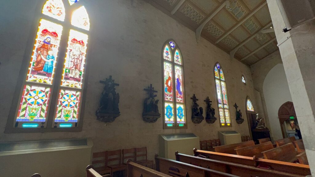 Stained-glass windows and wooden pews along the limestone nave wall inside San Fernando Cathedral
