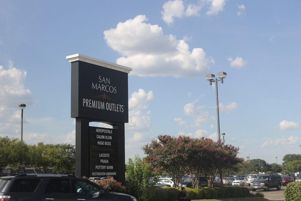 The tall black San Marcos Premium Outlets sign listing brand names above a parking lot with trees