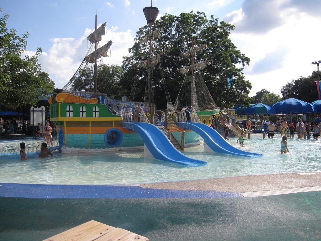 A children's splash pool with slides and a pirate-ship play structure under blue umbrellas at Schlitterbahn New Braunfels
