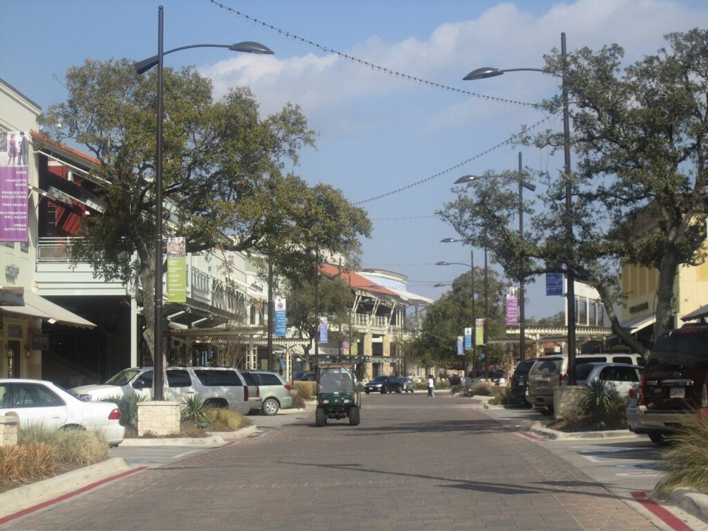 A tree-lined street of two-story shops with strings of lights overhead at the Shops at La Cantera