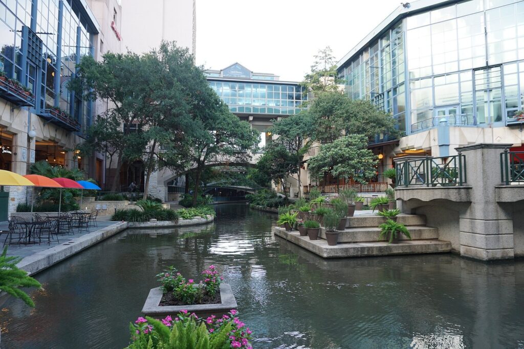The lagoon at the Shops at Rivercenter, with the River Walk's water, stone steps, flowers and glass-fronted mall buildings