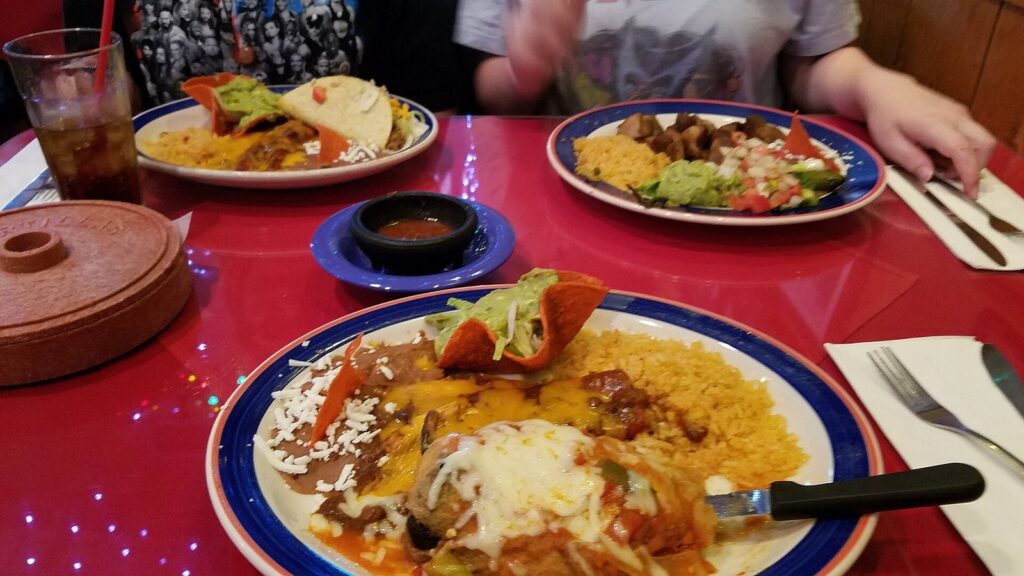 Tex-Mex combination plates with enchiladas, rice, beans and a crispy taco on a red table at Mi Tierra