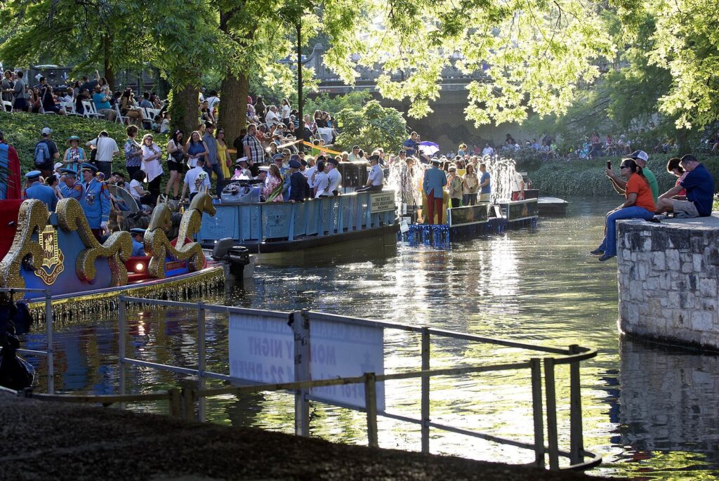 Crowds seated along the River Walk as decorated floats line up on the river before the Texas Cavaliers River Parade during Fiesta