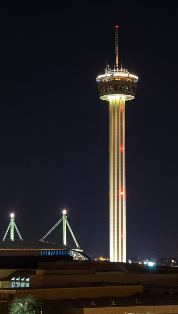 The illuminated Tower of the Americas rising into the night sky above Hemisfair, with its lit top deck