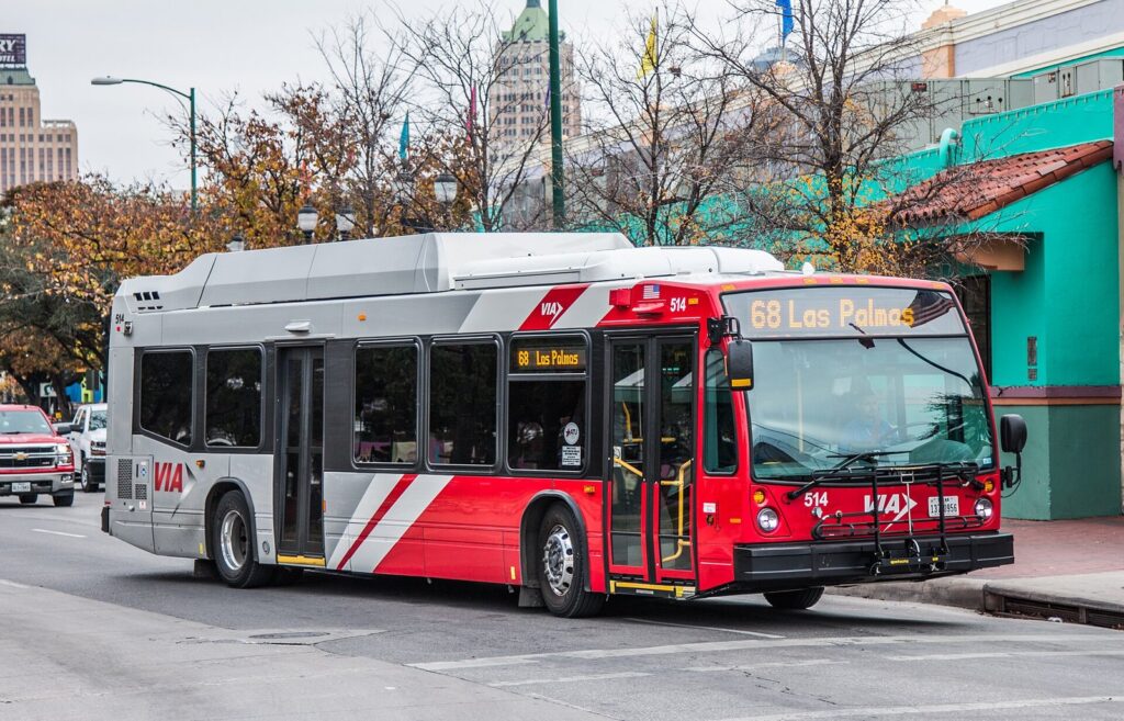 A red and silver VIA city bus pulling up at Market Square downtown, one practical answer to how to get around San Antonio without a car