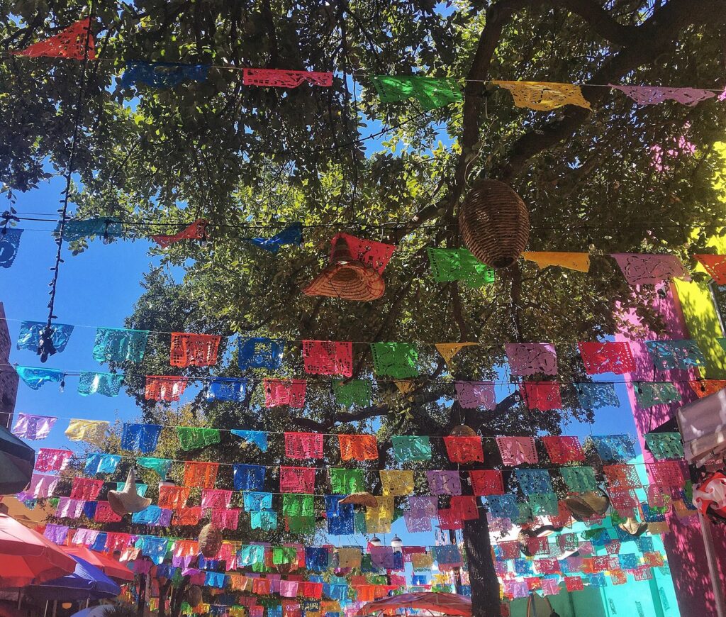 Rows of colorful papel picado banners strung through trees over a walkway at Historic Market Square in San Antonio