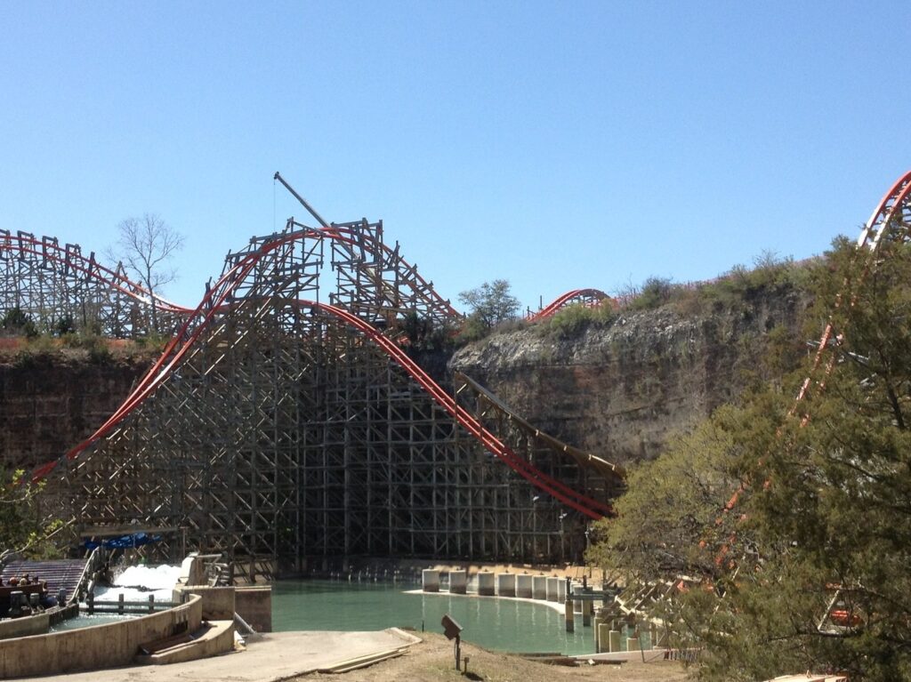 The red track of the Iron Rattler roller coaster curving over its wooden-style structure beneath the limestone quarry wall at Six Flags Fiesta Texas