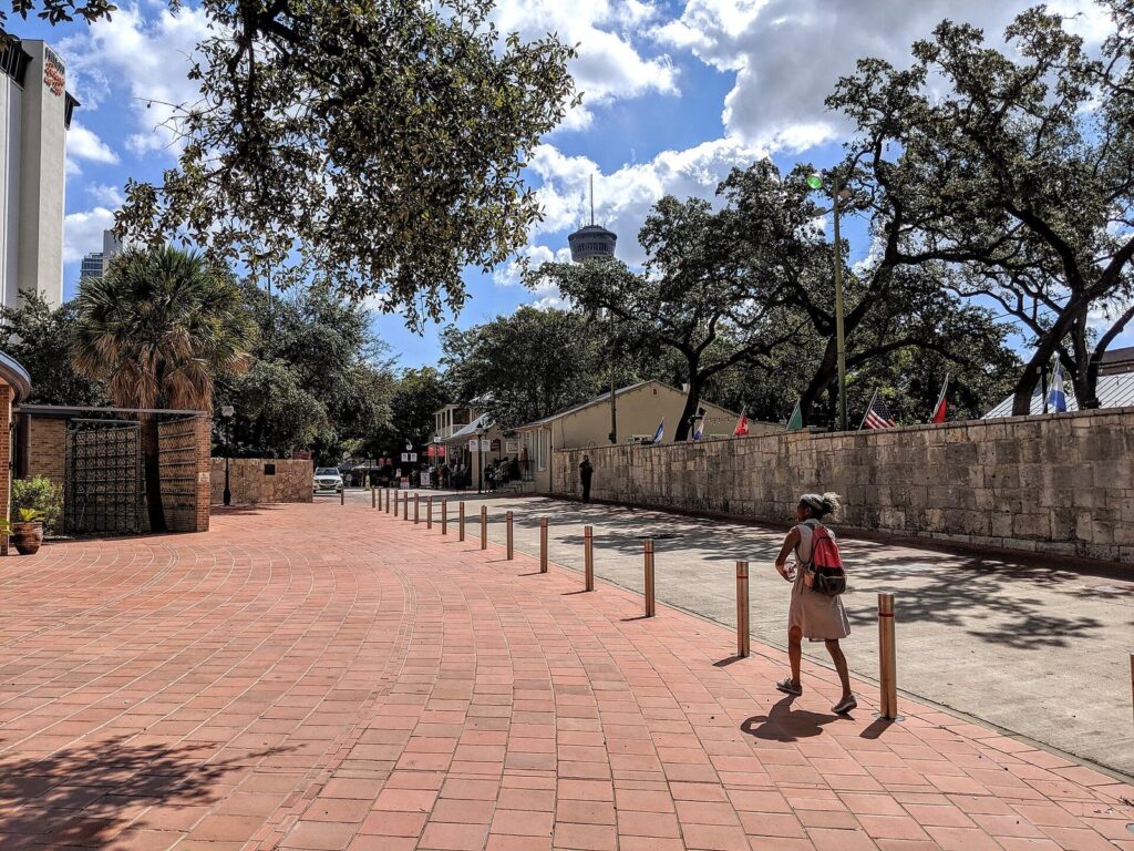 The brick-paved plaza of La Villita in San Antonio under live oaks, with the Tower of the Americas rising above the trees
