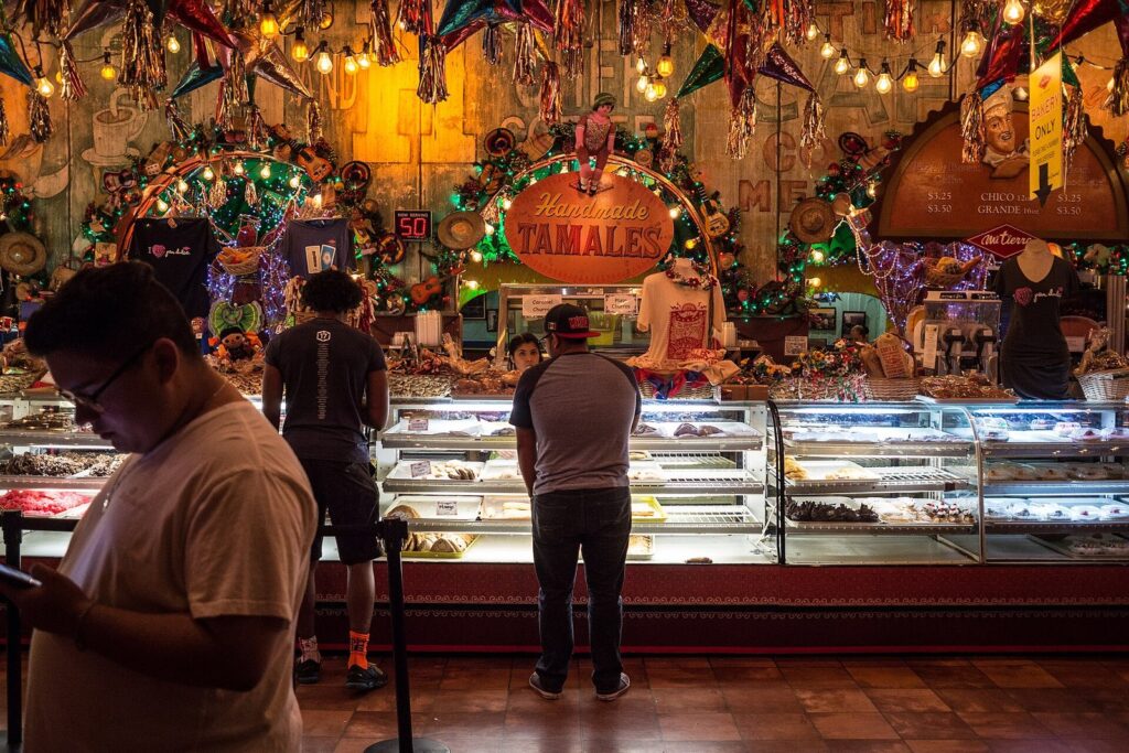 Customers at the long glass bakery counter at Mi Tierra Cafe in San Antonio, under strings of lights and colorful decorations