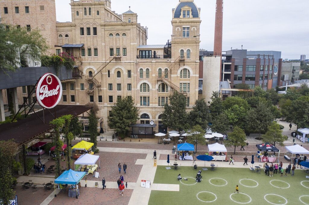 The Pearl's Saturday farmers market seen from above, with white and blue vendor tents on the plaza below the old brewhouse tower in San Antonio