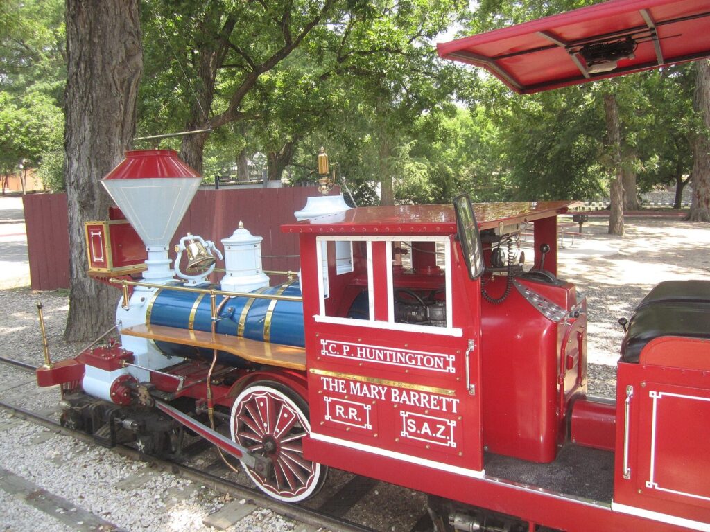 The red-and-blue engine of the San Antonio Zoo train, the C.P. Huntington, waiting on its track under shade trees